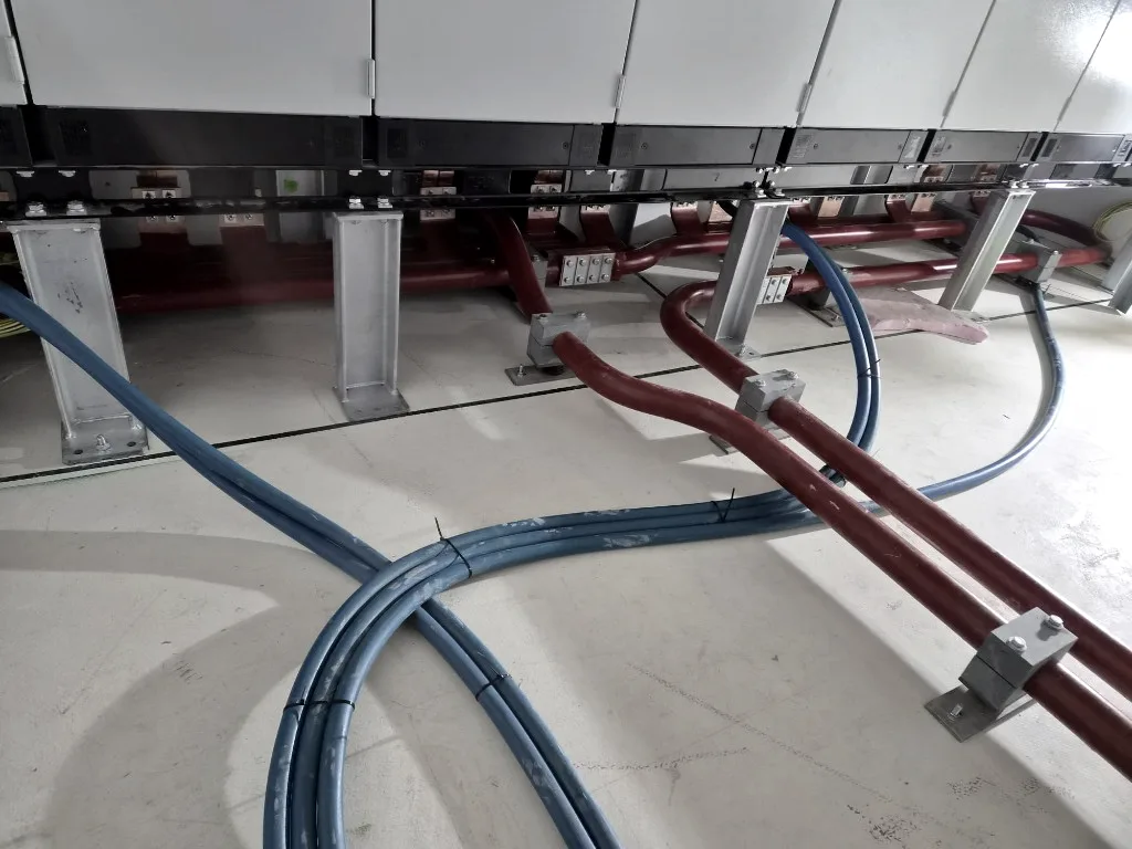 Rote und blaue Kabel unter einer Schaltanlage, auf dem Boden verlegt und befestigt